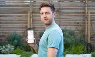 Мъж, показващ телефона си с приложението Dexcom и сензора Dexcom ONE на ръката си